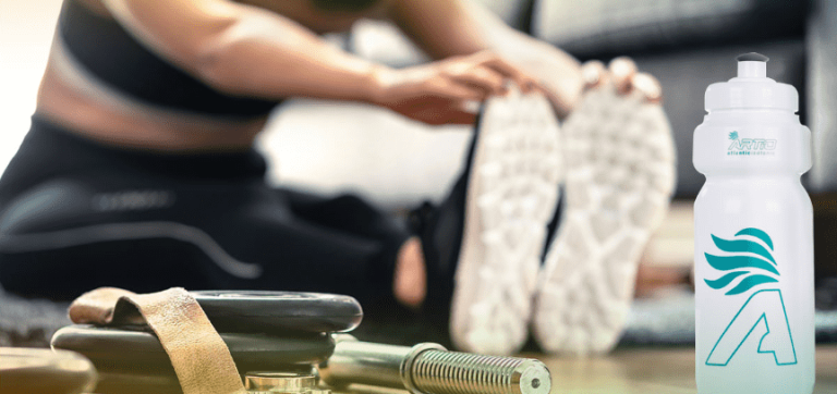 Mujer estirando en un gimnasio junto con nuestra bebida isotónica natural Artio